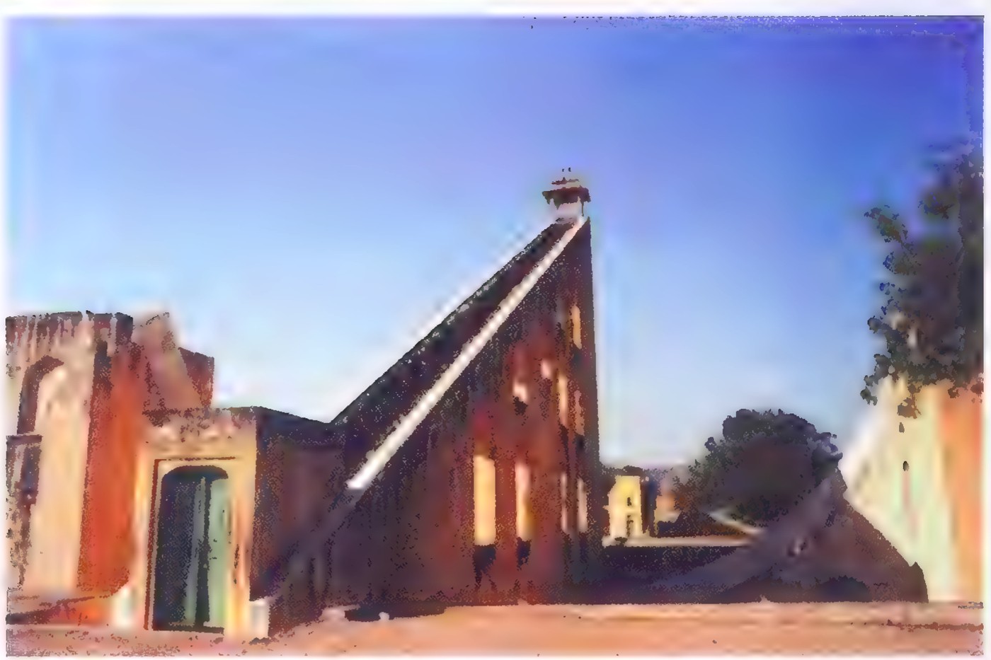 Photograph of the Jantar Mantar sundial in Jaipur, India: a tall masonry ramp with a staircase edge rising above the surrounding buildings.