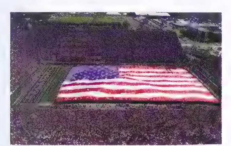 Aerial photograph of a huge United States flag laid out on the ground, with a road and fields around it.