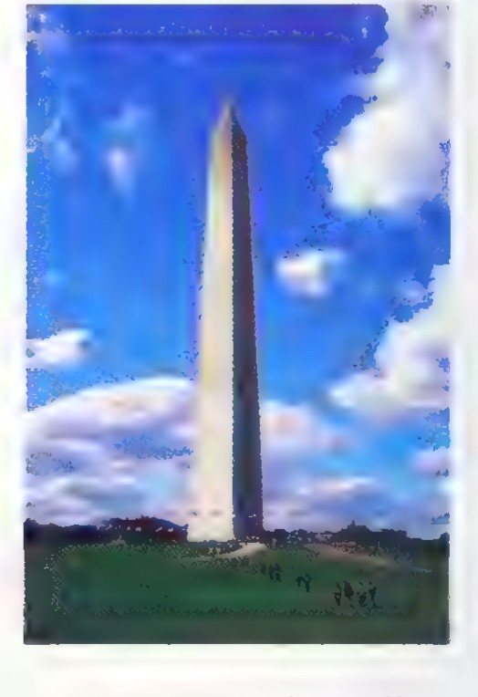 Photograph of the Washington Monument: a tall white obelisk rising above grass and trees against a blue sky.