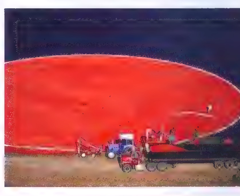 An aerial photograph of a huge circle of red cranberries floating on a dark bog, with harvesting equipment at the edge.