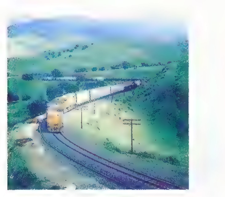 Photograph of a long freight train curving through a green valley, with the tracks bending smoothly out of sight.