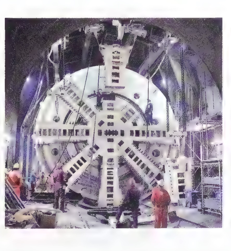 Photograph of a giant tunnel-boring machine: a huge circular cutting head with spokes standing in a shaft.